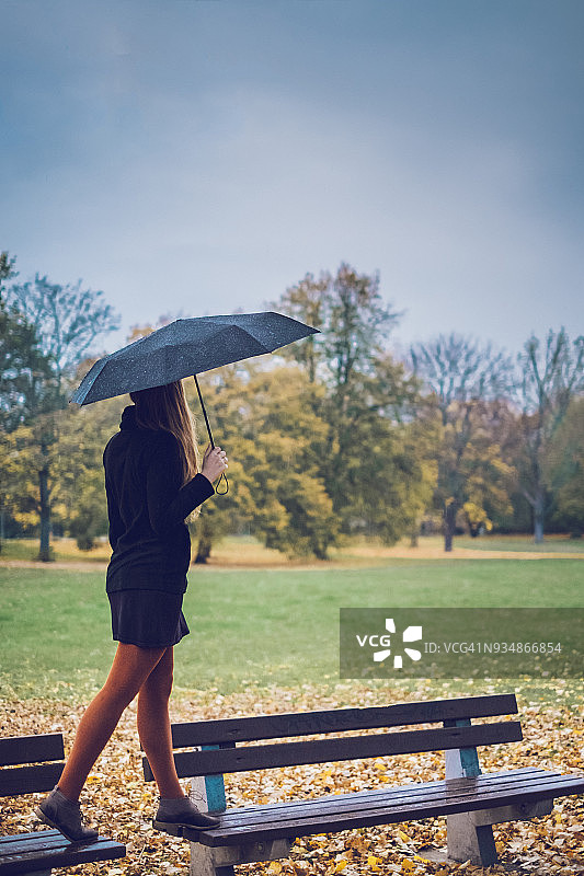 在秋天的公园里，年轻女子撑着雨伞站在两条长凳上图片素材