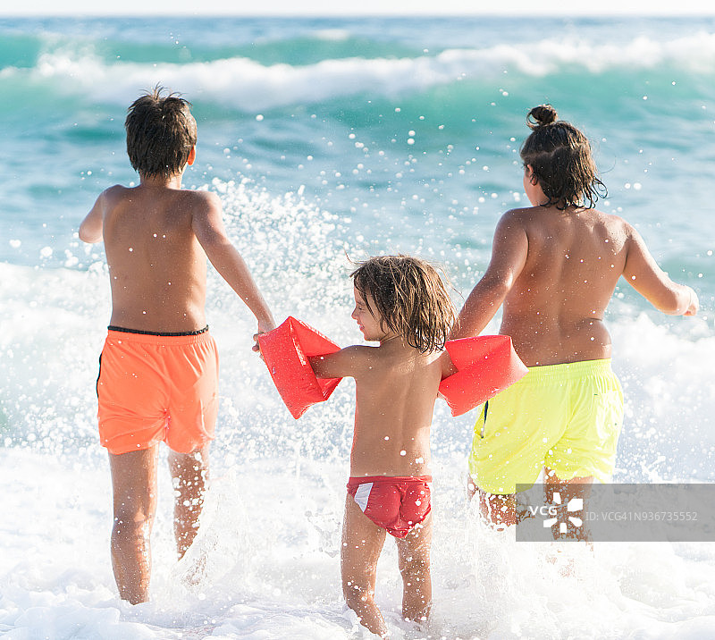 三个男孩在海滩上跑步和玩图片素材