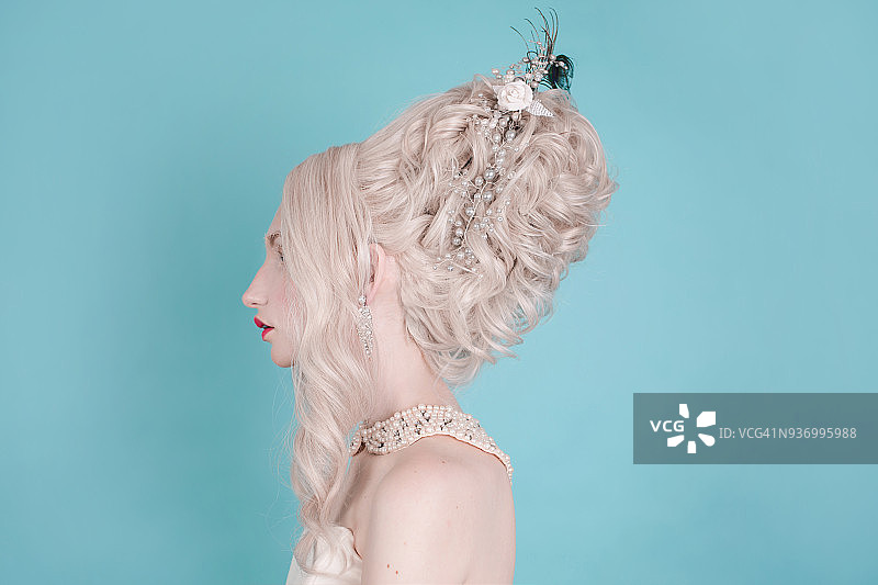 金发女人美丽奢华的洛可可式发型在白色的裙子在蓝色的背景图片素材