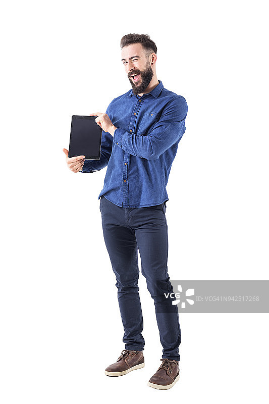 有趣的表情丰富的年轻胡子男子展示空白的平板电脑屏幕对着相机眨着眼图片素材