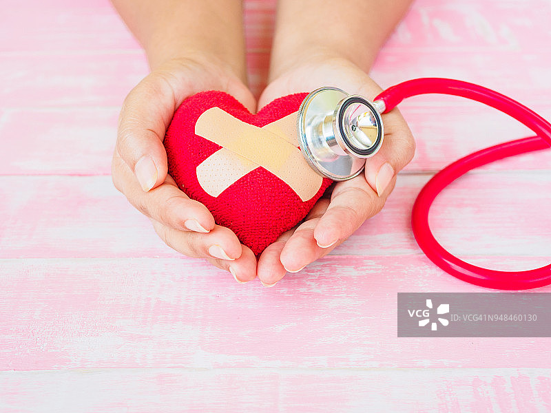 健康和医学，爱情和情人节的概念。红心在一个女人的手上，红色听诊器在粉红色的木头背景图片素材