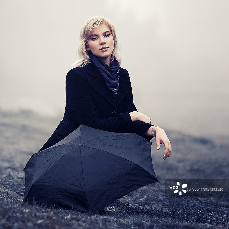 年轻时尚的女人撑着伞在雾中走在户外图片素材