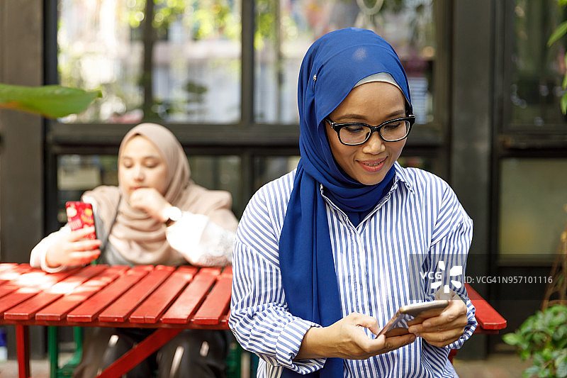 微笑的年轻穆斯林妇女在咖啡馆使用手机图片素材