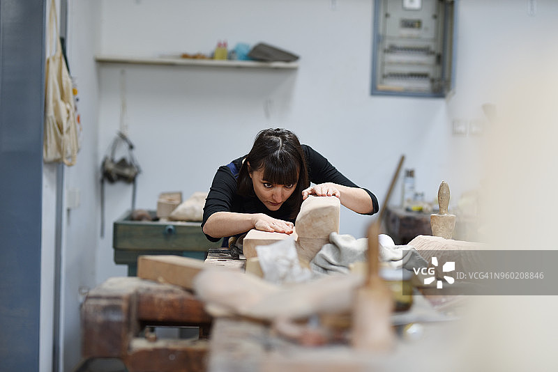 年轻的女雕塑家正在她的工作室里工作图片素材