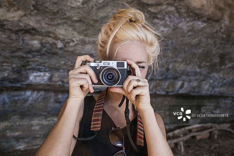 年轻女子通过老式相机在岩石上拍照图片素材