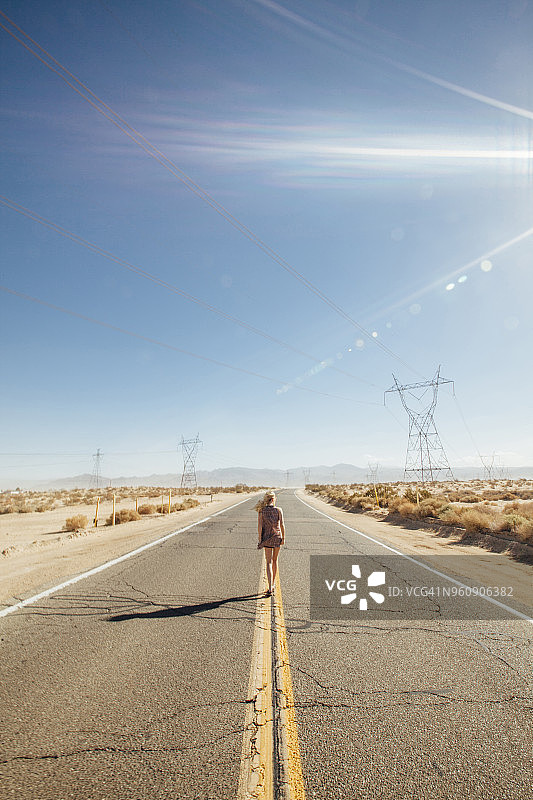 后视图的妇女走在道路上的沙漠在阳光明媚的一天图片素材