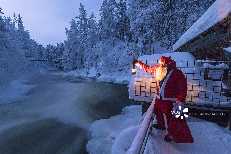 芬兰拉普兰库萨莫乌兰卡国家公园Juuma结冰的Myllykoski急流上，圣诞老人提着灯笼图片素材