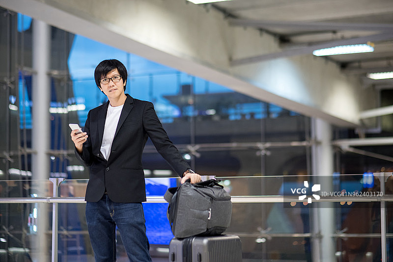 年轻的亚洲商人带着他的行李箱在机场候机厅等待图片素材