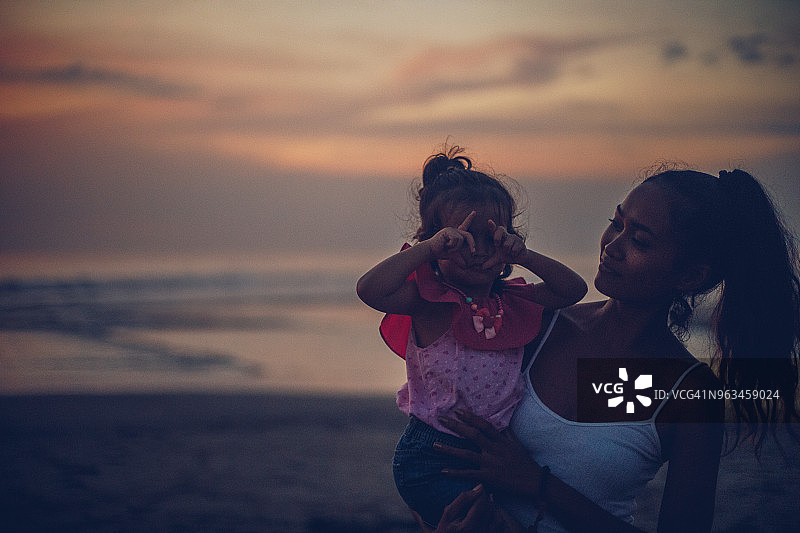母亲和可爱的女儿在海滩上欣赏日落图片素材