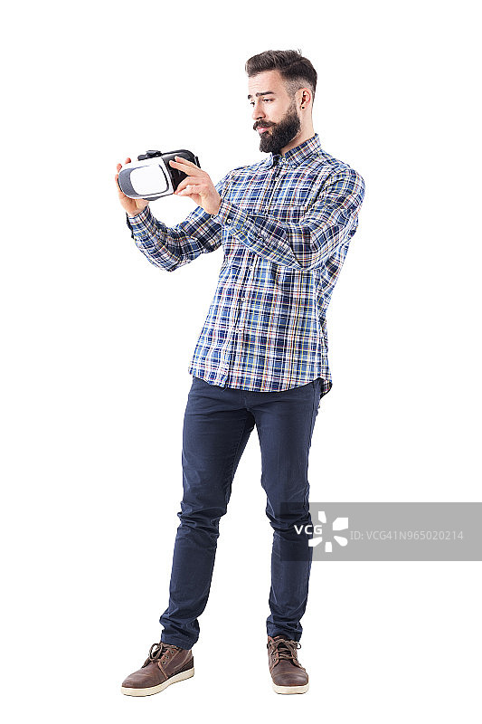 年轻的胡子商人拿着并检查虚拟现实头盔。图片素材