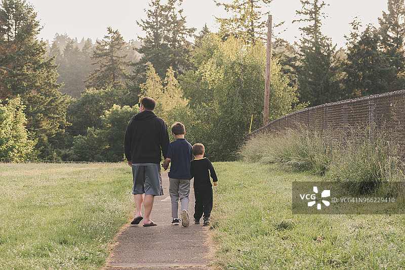 后视图的父亲和儿子走在小路上的草地对树木图片素材