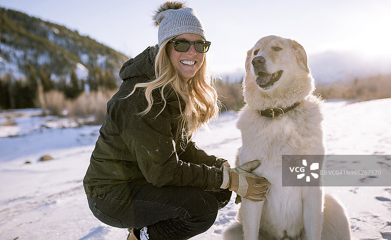 戴着太阳镜的快乐女人和狗在雪地上图片素材