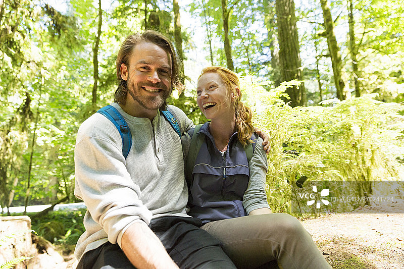 一对笑嘻嘻的情侣徒步旅行坐在森林里倒下的树上图片素材