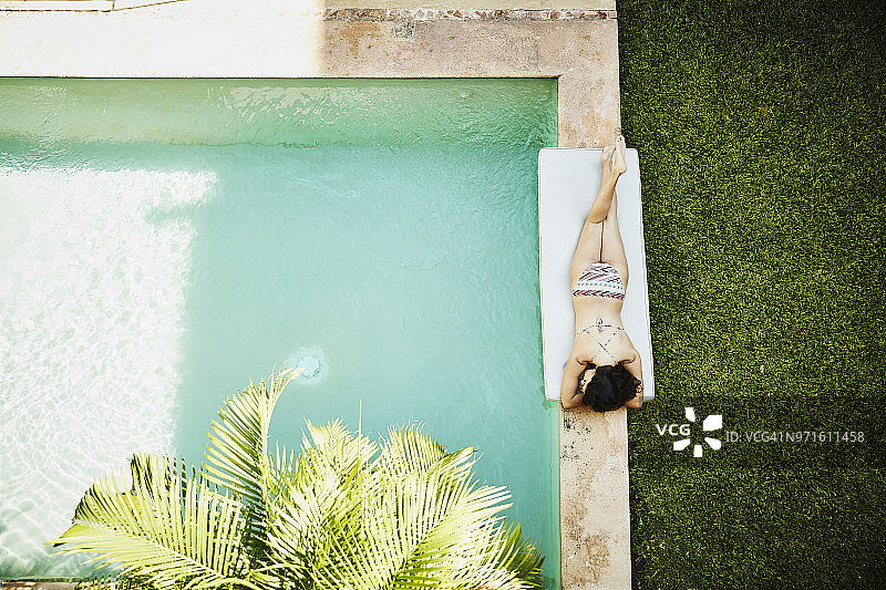 头顶上的女人躺在泳池旁边的庭院户外水疗中心图片素材