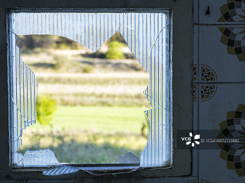 一个废弃的窗户与玻璃破碎的房子的特写，以田野的观点。图片素材
