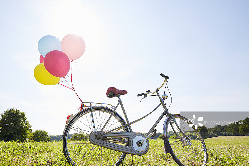 骑着彩色气球的自行车在草地上对着天空图片素材