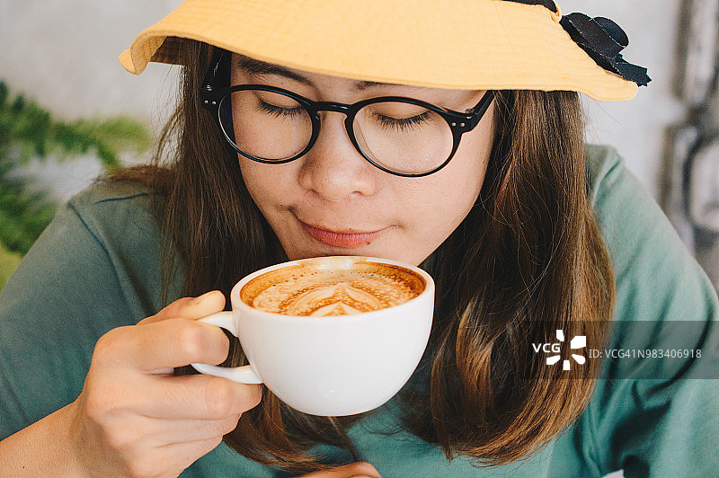 近距离观察亚洲女性在咖啡馆喝热拿铁咖啡。图片素材