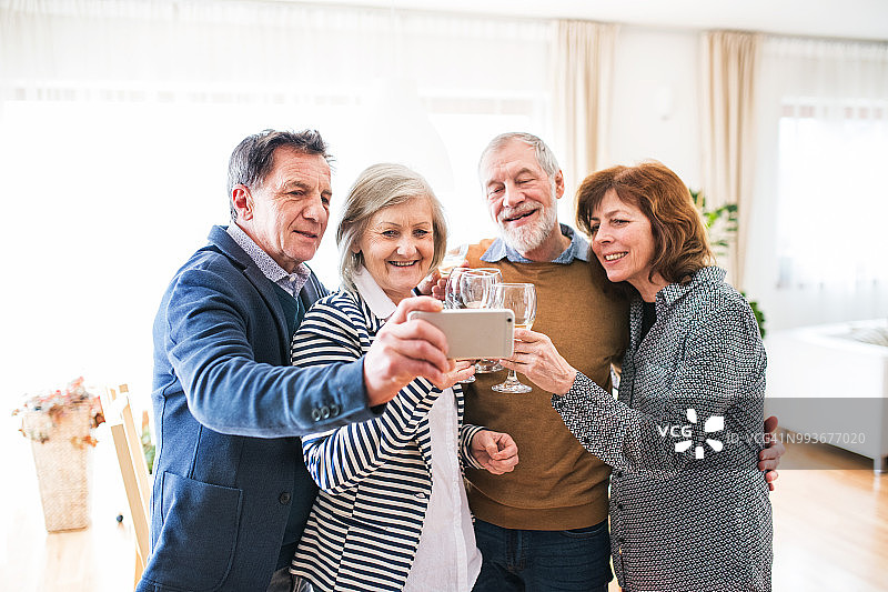 朋友在家里拿着白葡萄酒酒杯的照片。老年人用智能手机自拍。图片素材