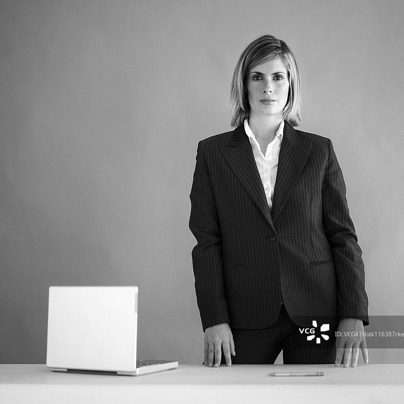 一个拿着笔记本电脑站在桌子后面的女商人图片素材