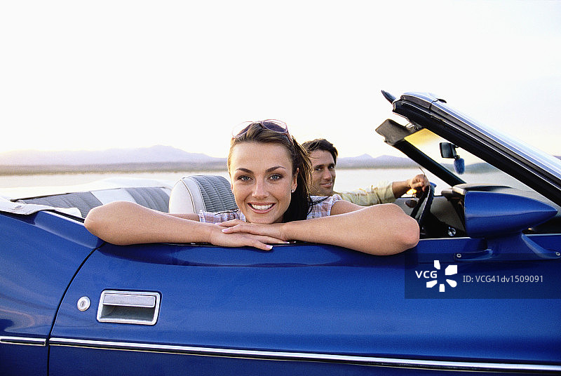 一对夫妇开着一辆蓝色敞篷车穿越沙漠，女人靠在车门上图片素材