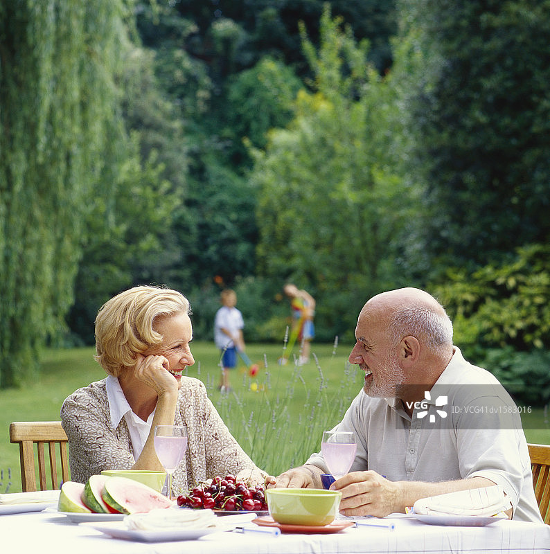 老夫妇坐在桌子旁，孩子们在后面的花园里玩槌球图片素材