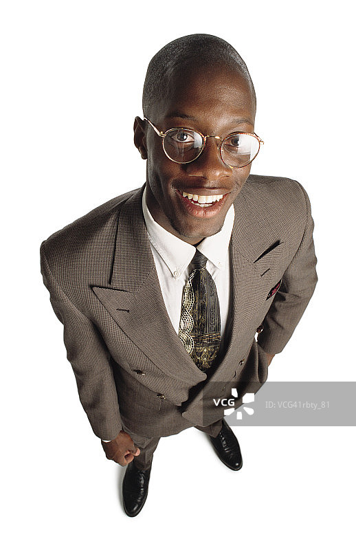 一位身穿灰色西装、黑色皮鞋、系着白衬衫和领带的非裔美国人抬起头微笑着把手伸进口袋图片素材