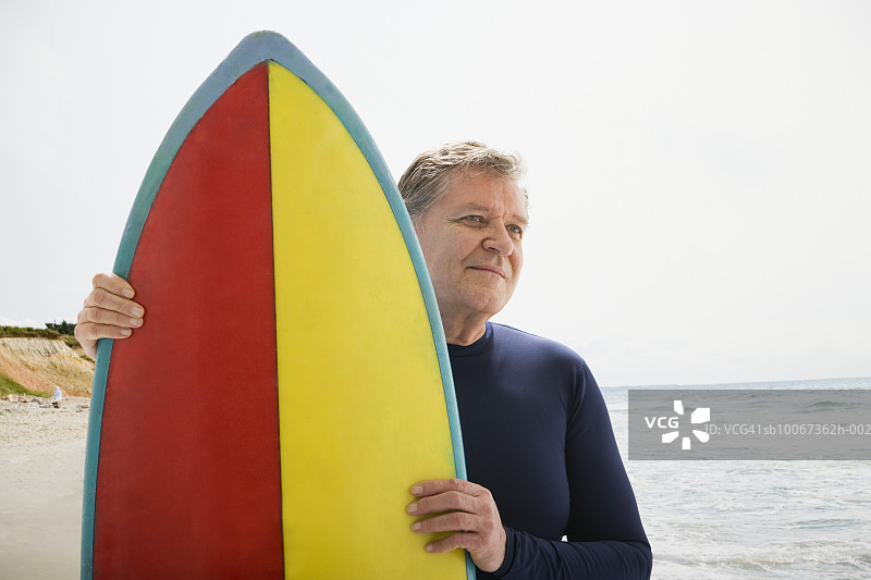 成熟的男人在海滩上拿着冲浪板，微笑着图片素材