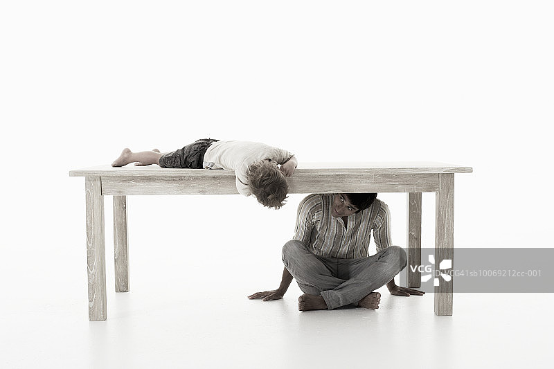 男人坐在桌子下和儿子玩耍(4-5年)，在摄影棚拍摄图片素材