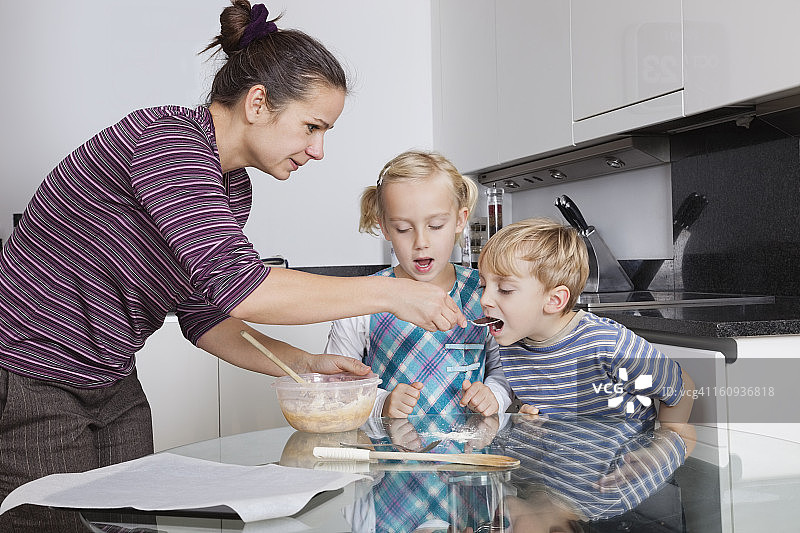 母亲和孩子们在厨房烘焙和品尝饼干面糊图片素材