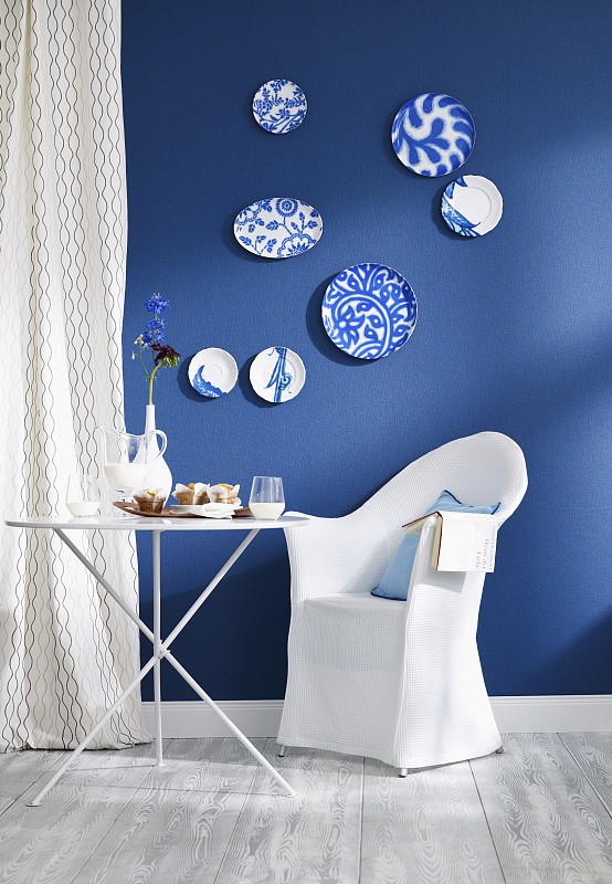 蓝色的墙壁上装饰着各种盘子，有折叠桌和安乐椅图片下载
