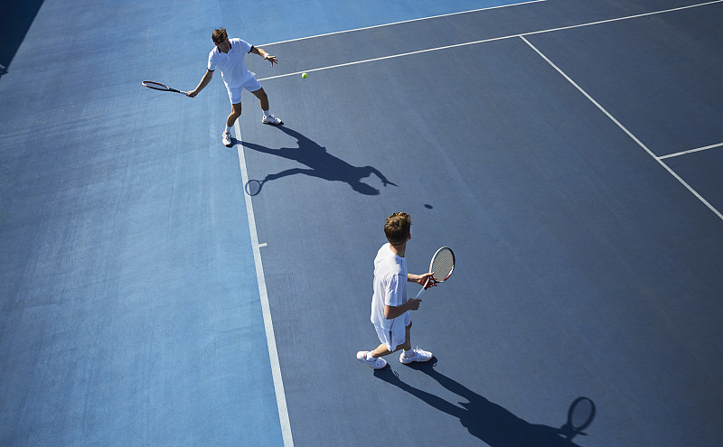年轻男子双打网球运动员在阳光明媚的蓝色网球场上打网球图片下载