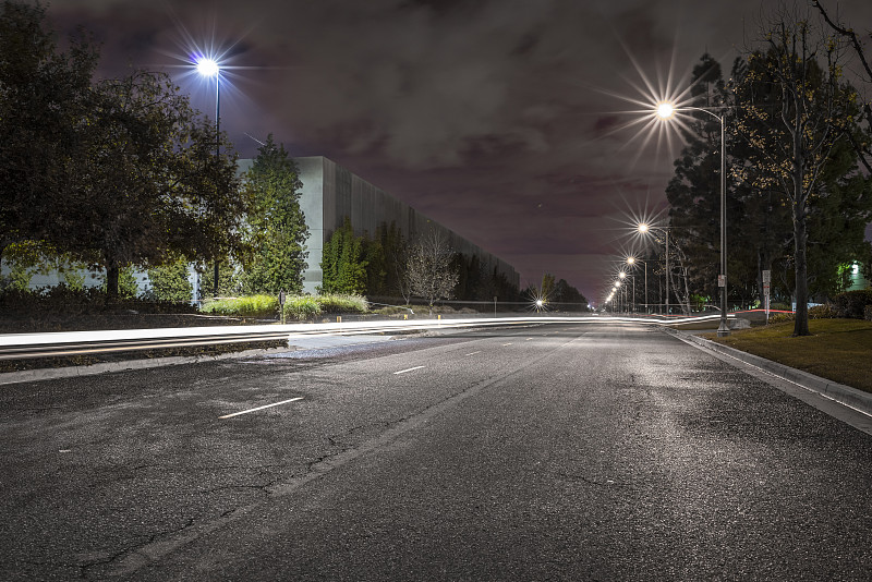 在美国圣菲斯普林斯，夜晚有路灯和现代化仓库的绿树成荫的道路图片下载
