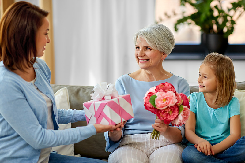 家庭，世代和生日快乐，母亲和女儿在家里给祖母送花和礼物。女性家庭赠送礼物给祖母图片下载