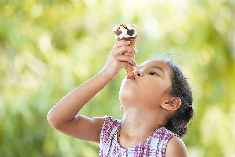 可爱的女孩坐在公园里靠树吃冰淇淋的特写图片素材