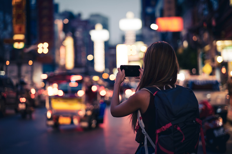 一名背包客在夜间用手机拍摄曼谷的瑶瓦拉特路。泰国图片素材