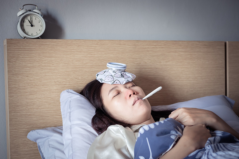 亚洲妇女感冒高烧，睡在舒适的床上使用冰袋受伤减少和使用温度计测量温度。生病在家图片下载