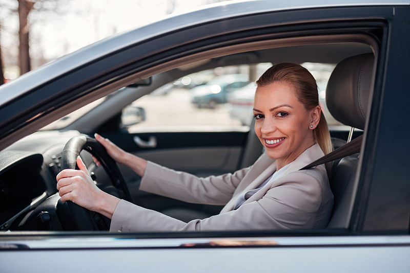 一个美丽快乐的女人驾驶着一辆车，对着镜头微笑的肖像。图片下载