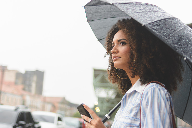 一名年轻女子在雨天用智能手机等出租车图片下载