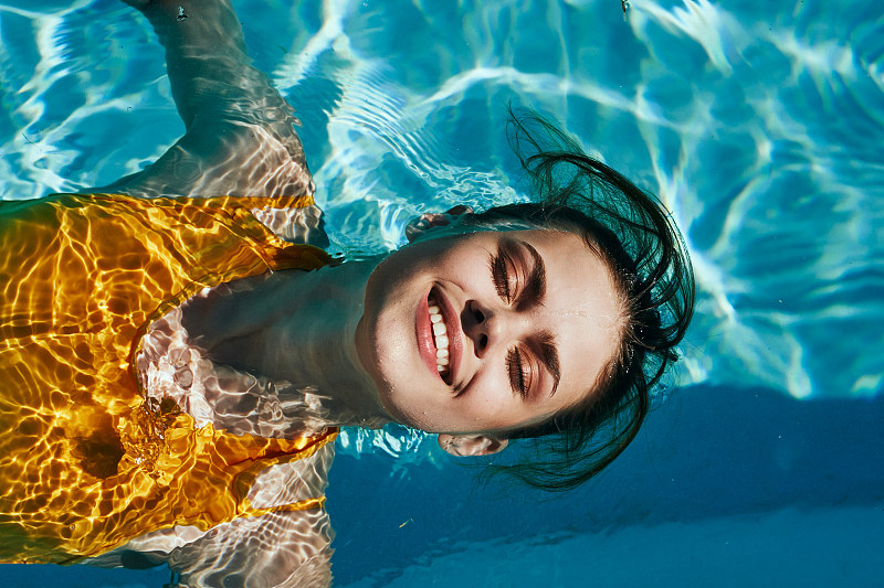 漂亮的女孩穿着黄色的泳衣，微笑着在游泳池里游泳图片下载