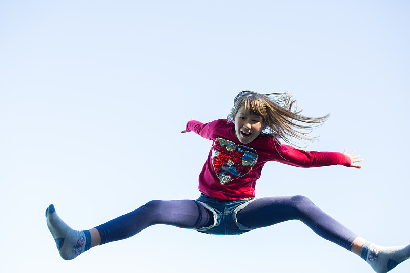 9-10岁的漂亮女孩跳上了外面的蹦床，玩得很开心图片下载
