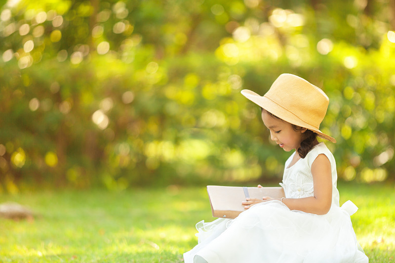 坐在公园里看日记的可爱女孩图片素材
