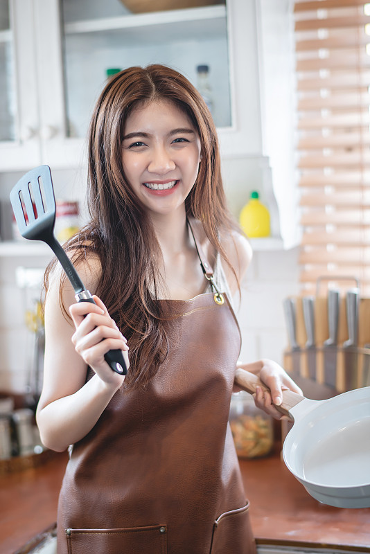 微笑的年轻妇女拿着厨房用具的肖像图片素材