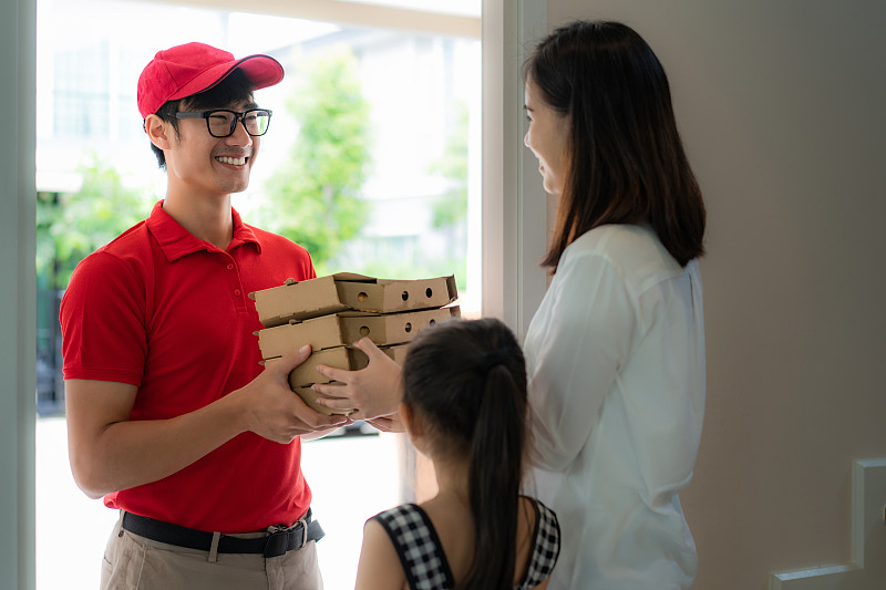 亚洲男子送披萨食物在纸盒亚洲妇女和她的女儿客户在家。图片下载