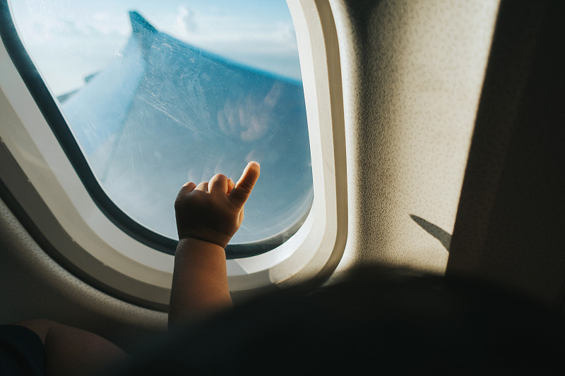 一个蹒跚学步的孩子在旅行时用手指着飞机窗户对着蓝天图片下载