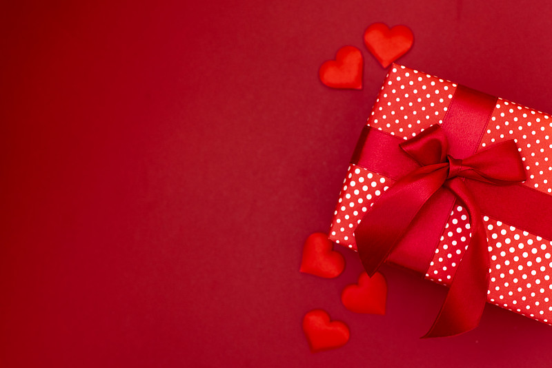 一个礼物在牛皮纸盒与一个红色的蝴蝶结在红色的背景与心。给你的爱人一个惊喜。情人节的概念有婚礼、生日、新年、圣诞节等节日图片下载