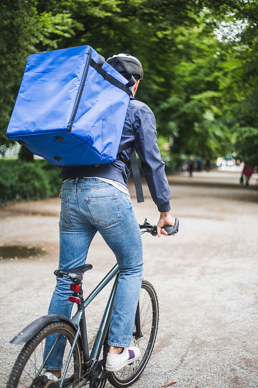 在城市街道上骑自行车的送餐员的后视图图片下载