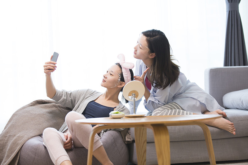 两个青年女子在客厅美容护肤贴面膜拿着手机自拍合照图片素材