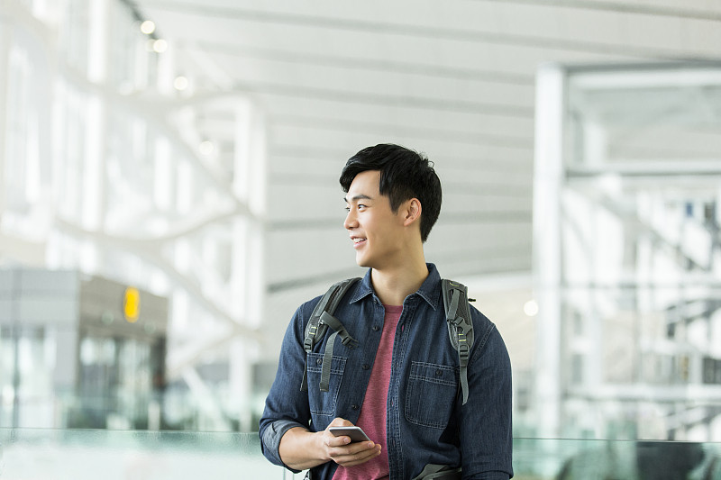 青年男子背着包使用手机在机场等候图片下载