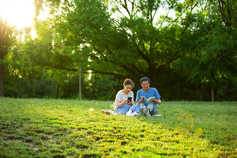 老年夫妻在户外公园野餐看书看手机图片下载
