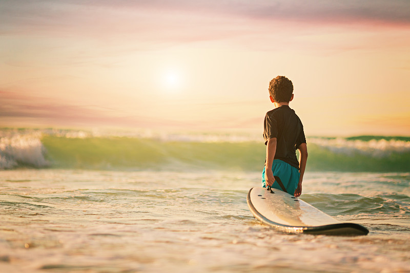 一个冲浪男孩抱着冲浪板看海浪的背影图片下载